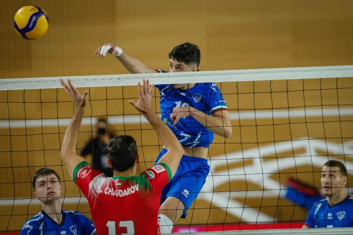 Volleyball players at the net: a blue-team spiker jumps to spike the ball while a red-team blocker rises to block.