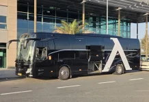 Левски пристигна в Германия, продължава към Нидерландия за мача с НЕК Black luxury tour bus with a large white A design on its side, parked in front of a glass-fronted building.