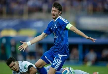 В Левски притеснени за Кристиан Димитров Male soccer player in blue kit with a captain's armband stretches his arms during a match, while a white-uniform opponent lies on the ground nearby.