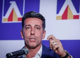 Левски ще заложи на бразилци през зимата Man in a dark suit speaks into a microphone at a podium, gesturing with his hand during a public event with a blue-and-white backdrop and logos behind him.