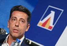 Левски сменя курса: „сините“ вдигат нивото на селекцията Man speaking into a microphone at a conference, with a blue backdrop and a geometric logo nearby