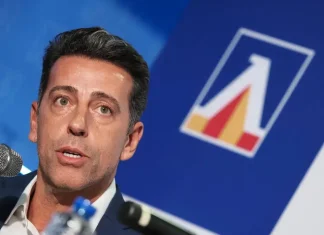 Левски сменя курса: „сините“ вдигат нивото на селекцията Man speaking into a microphone at a conference, with a blue backdrop and a geometric logo nearby