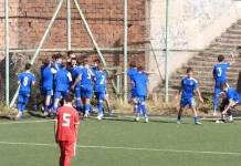 Левски U14 надви ЦСКА на „Герена“ Young soccer players in blue celebrate near the goal on an outdoor field; a red player with number 5 stands in the foreground facing away from the group.