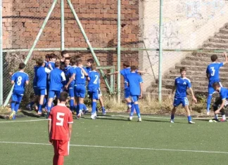 Левски U14 надви ЦСКА на „Герена“ Young soccer players in blue celebrate near the goal on an outdoor field; a red player with number 5 stands in the foreground facing away from the group.