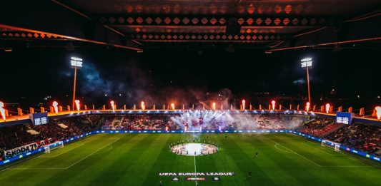 Левски с важни указания към феновете преди мача с Виктория Пилзен Nighttime UEFA Europa League stadium celebration: circular center-circle display with players around the emblem, flames and smoke in stands, full stands.