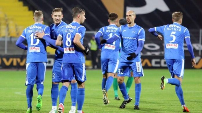 Seven soccer players in blue uniforms walk together on a well-lit grass field after a match.