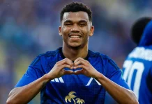 Майкон: кариера, отбори и факти Soccer player in a blue jersey smiling while forming a heart shape with his hands on the field.