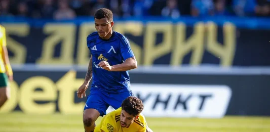 Майкон сбъдна детска мечта с Левски Soccer clash: a blue-team player challenges a yellow-team defender for the ball on a sunlit field, both near the ball.