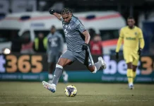 Макун се прибира по-рано в Левски след лагера на Венецуела Soccer player in a gray kit mid-kick, striking the ball on a grass field with a yellow-clad goalkeeper in the background.