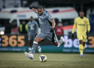 Макун се прибира по-рано в Левски след лагера на Венецуела Soccer player in a gray kit mid-kick, striking the ball on a grass field with a yellow-clad goalkeeper in the background.