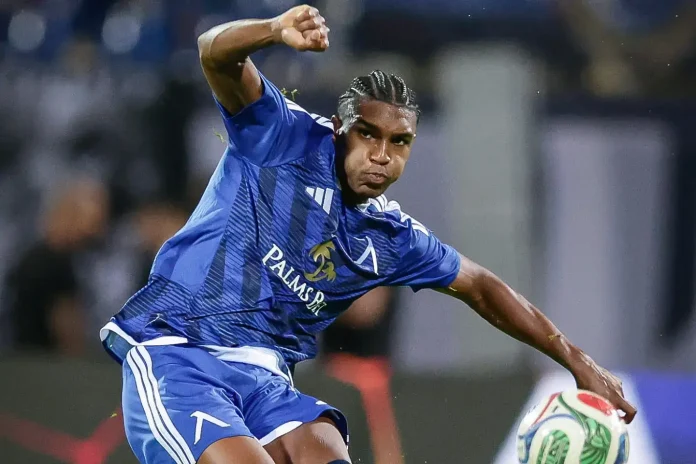 Soccer player in a blue Palmeiras jersey kicking a ball mid-action during a match, with braided hair