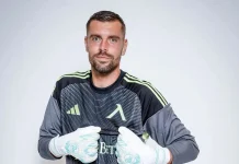 Мартин Луков – мачове, голове и кариера Male soccer goalkeeper wearing a dark jersey with lime-green stripes, posing with gloved hands held near his chest against a light background.