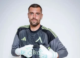 Мартин Луков – мачове, голове и кариера Male soccer goalkeeper wearing a dark jersey with lime-green stripes, posing with gloved hands held near his chest against a light background.