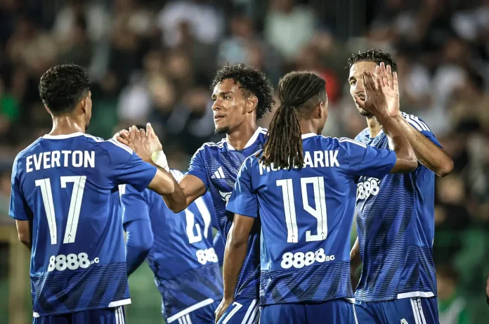 Soccer players in blue jerseys celebrate with high-fives on the field, crowd in the stands behind them.