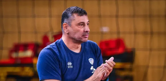 Николай Желязков след четвъртата поредна Суперкупа на Левски: Показахме характер в най-важния момент Coach or team staff member in a blue T-shirt clapping in an indoor sports venue, with red seats in the background.