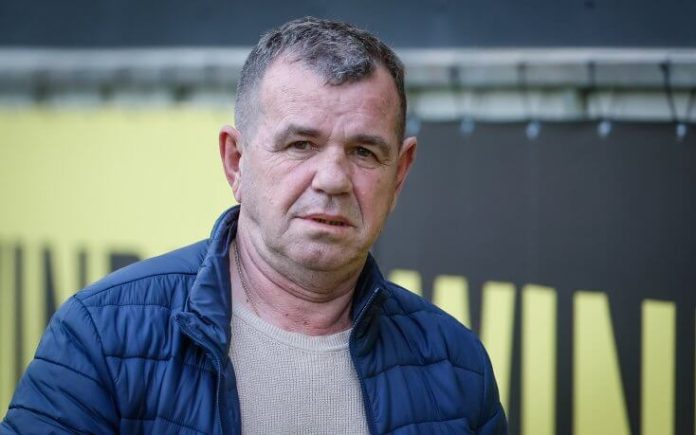 Middle-aged man with short gray hair wearing a blue puffer jacket, looking at the camera outdoors.