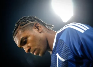 Самсунспор не се отказва от Макун Profile view of a male athlete with cornrow braids in a blue jersey, illuminated by bright stadium lights.