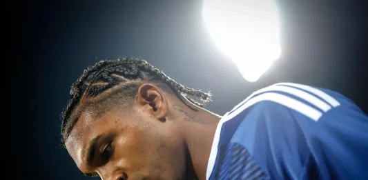 Самсунспор не се отказва от Макун Profile view of a male athlete with cornrow braids in a blue jersey, illuminated by bright stadium lights.