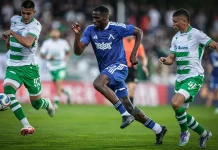Сангаре пак се контузи, „сините“ мислят за нов нападател Blue-team player in mid-run dribbles the ball while two green-and-white striped players pursue him on a soccer field.
