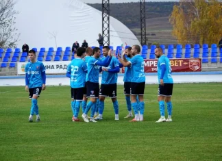 Струмска слава измъкна точка срещу дубъла на Левски Soccer players in blue kits form a huddle on a green field before a match with empty blue seats behind them.