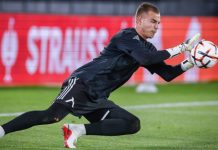 Светослав Вуцов Левски оглави престижна класация Soccer goalkeeper in a black kit diving to his left, reaching for a ball near the goal line on a green pitch with red advertising boards in the background.