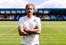 Треньорът на Виктория Пилзен: Знаем слабите места на Левски Male soccer coach standing on a grassy pitch with folded arms, wearing a white polo shirt and a watch, empty stadium seating in the background.