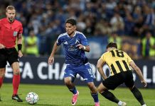 УЕФА глоби Левски и АЕК след плейофите в Шампионската лига Soccer player in a blue kit dribbles the ball past a yellow-and-black opponent as a referee watches from the left.