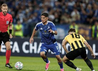 УЕФА глоби Левски и АЕК след плейофите в Шампионската лига Soccer player in a blue kit dribbles the ball past a yellow-and-black opponent as a referee watches from the left.