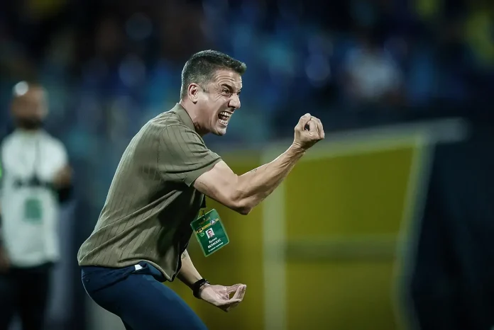 Coach on the sidelines celebrating with a raised clenched fist during a game.