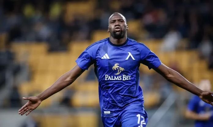 Soccer player in a blue kit with arms outstretched, celebrating on the field; Palms Bet sponsor on jersey.