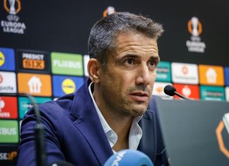 Веласкес готви сериозни промени в Левски за НЕК Man in a blue suit speaks into a microphone at a press conference with sponsor banners in the background