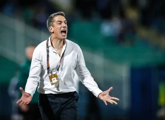 Веласкес пред юбилей с Левски Coach in a white shirt shouts with arms outstretched on a sports field, wearing a lanyard and pass attached to it.