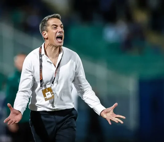 Веласкес пред юбилей с Левски Coach in a white shirt shouts with arms outstretched on a sports field, wearing a lanyard and pass attached to it.