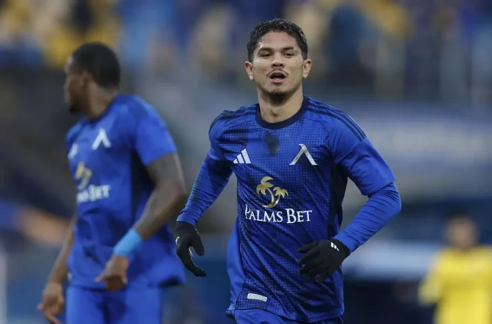 Soccer player in a blue kit sprinting on the field with the sponsor 'Palms Bet' logo visible on the chest.