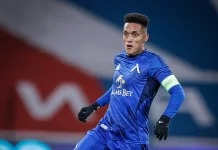 Вендерсон Цунами – история, отбори, награди и факти Blue-clad football goalkeeper in action, wearing a captain's armband and gloves during a match in front of a blurred background.