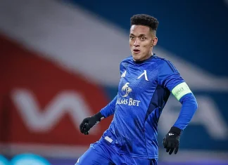 Вендерсон Цунами – история, отбори, награди и факти Blue-clad football goalkeeper in action, wearing a captain's armband and gloves during a match in front of a blurred background.