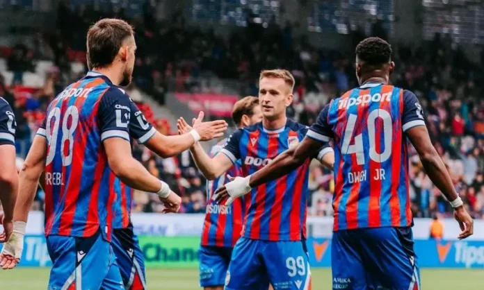 Soccer players in red-and-blue striped jerseys high-fiving on the field during a match celebration.