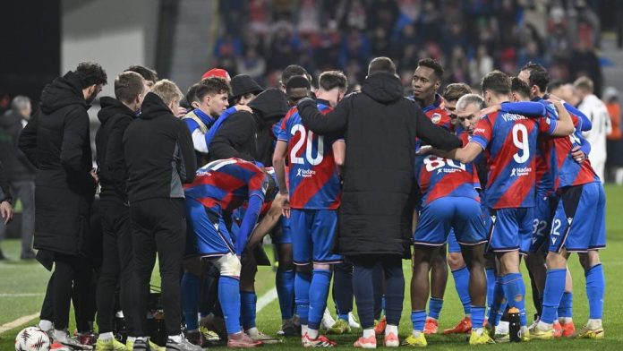 Soccer team in blue and red uniforms huddles together on the field before a match.