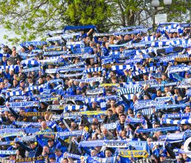 Large crowd of soccer fans in blue and white scarves cheering at a stadium; many scarves say Levski Sofia.