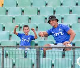 Man and boy in matching blue shirts posing and smiling among teal stadium seats.